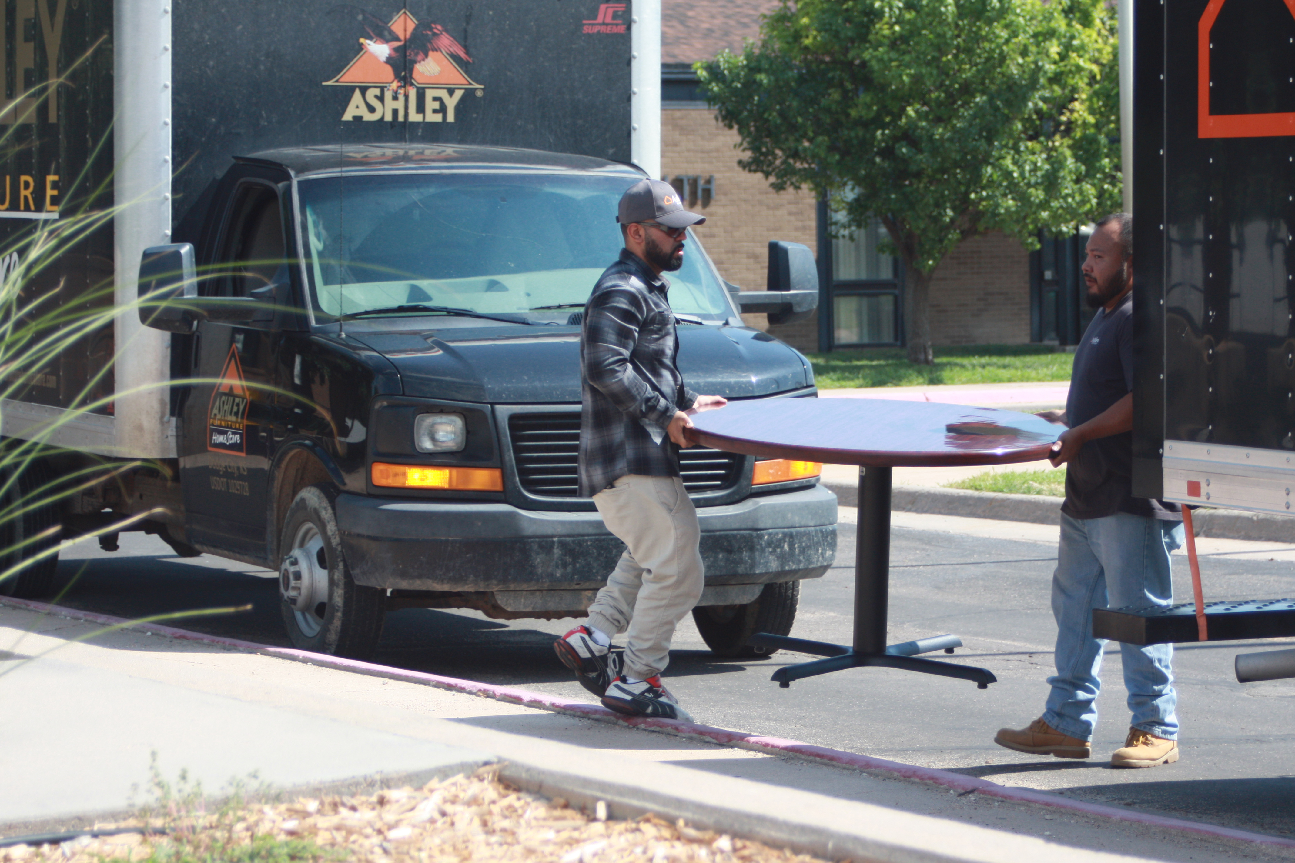 Employees of Ashley Furniture HomeStore carrying at table onto campus