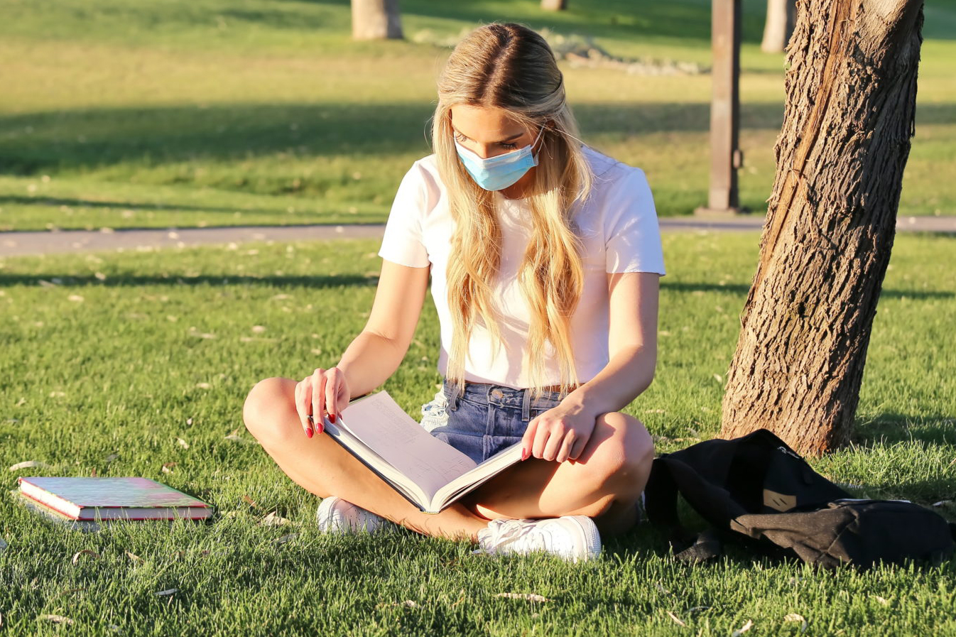 Student outside on campus wearing a mask while reading
